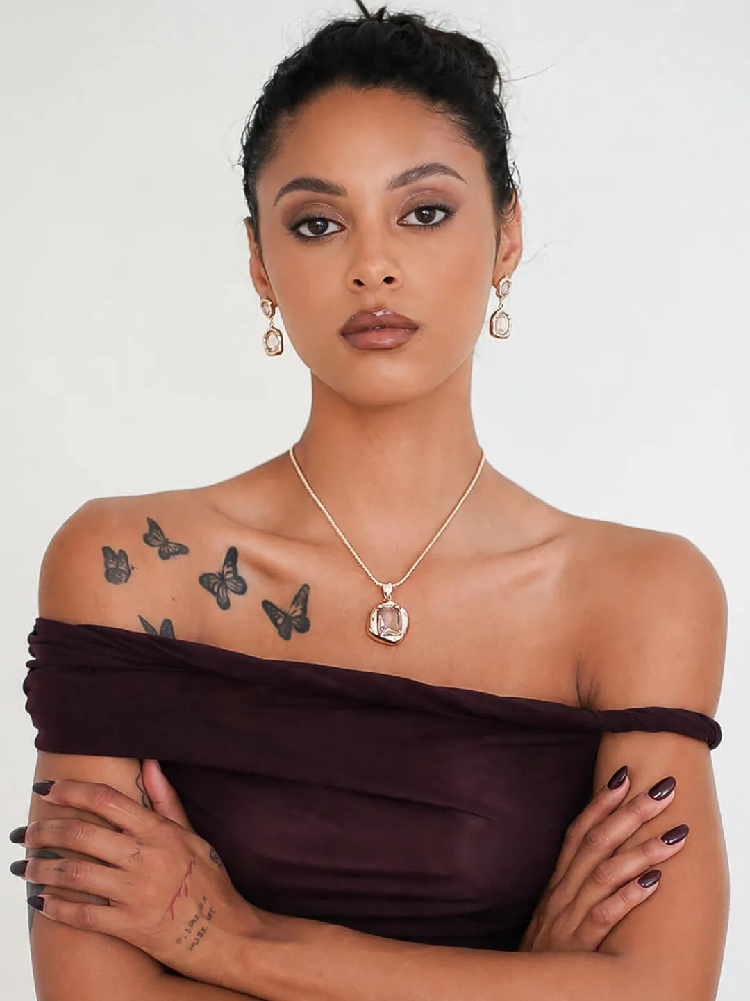 Model in an off-shoulder top wearing a gold pendant necklace and drop earrings