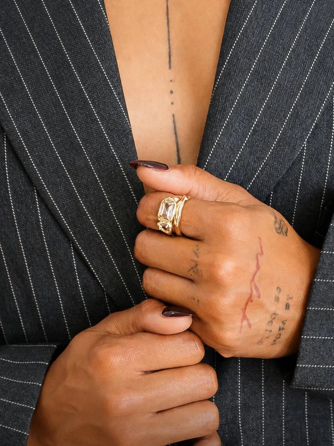 Hands holding a pinstripe blazer closed, wearing stacked gold rings